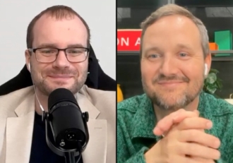 Two men on a split-screen video call: left, a man with glasses and a beige blazer speaks into a microphone; right, a man in a green shirt smiles with hands clasped.