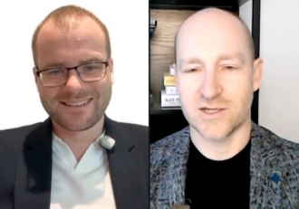 Split-screen video call: left is a smiling man in a suit with glasses and a lavalier mic; right is a bald man in a patterned blazer speaking.