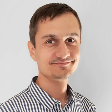 Smiling man with short dark hair in a striped button-down shirt, facing the camera against a light gray background