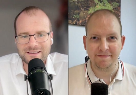 Split-screen video call with two men: left, wearing glasses and a white shirt, speaking into a microphone; right, in a polo shirt with earphones, smiling into a microphone.