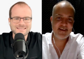 Split-screen video call: left man in glasses speaking into a microphone, right man in a white shirt with earbuds smiling.