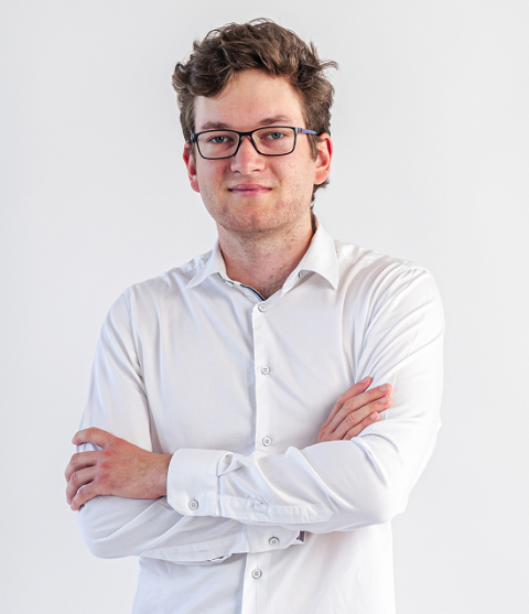 Head-and-shoulders portrait of a man with glasses in a white button-down shirt, arms crossed, against a plain light background.