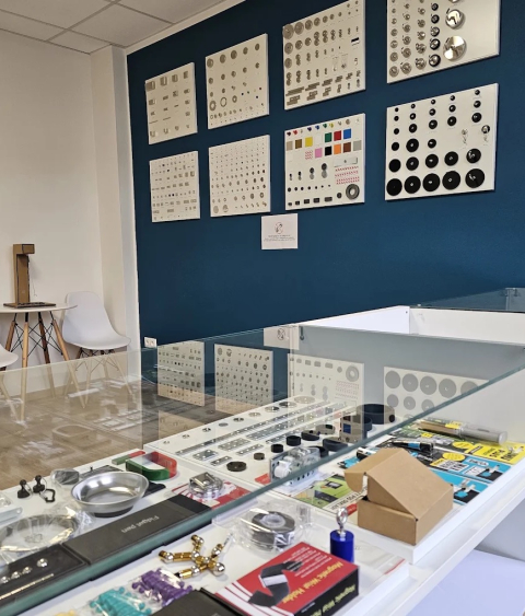 Showroom scene with a blue wall displaying white boards of circular metal components; glass display counter with tools and items in front.