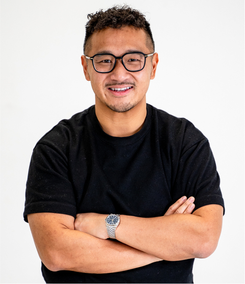 Man with glasses and a black t‑shirt smiling, arms crossed, wearing a silver watch.