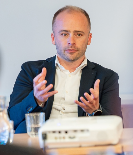 Businessman in a dark suit explains a point, using animated hand gestures during a meeting.